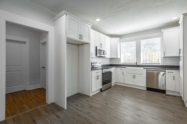 kitchen with appliances with stainless steel finishes, white cabinetry, dark wood-type flooring, tasteful backsplash, and sink