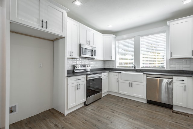 kitchen with white cabinets, sink, hardwood / wood-style flooring, appliances with stainless steel finishes, and decorative backsplash