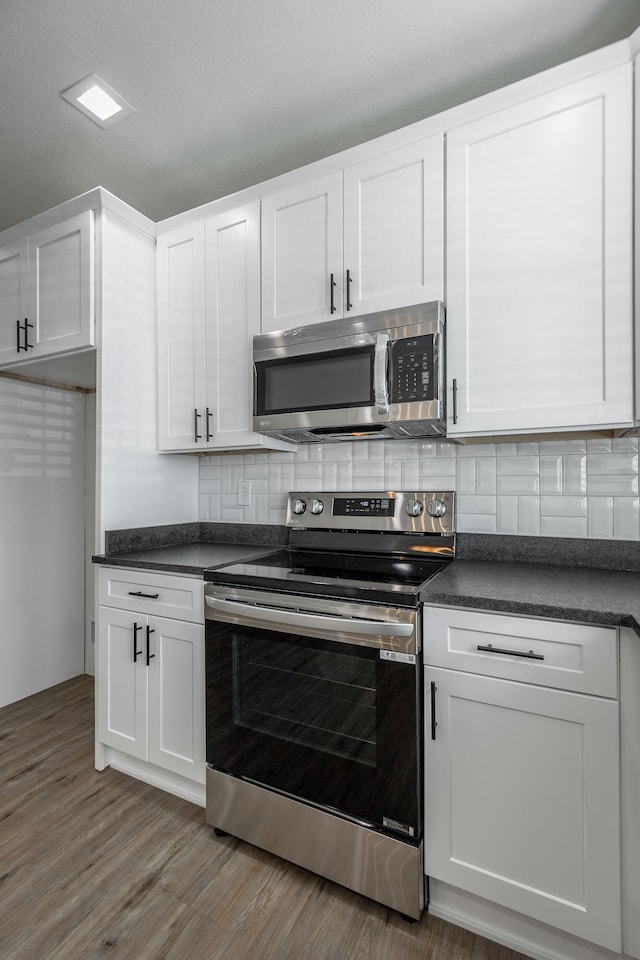 kitchen with tasteful backsplash, a textured ceiling, white cabinetry, hardwood / wood-style flooring, and appliances with stainless steel finishes