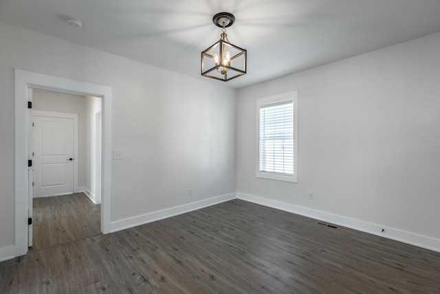 empty room with dark wood-type flooring and a notable chandelier