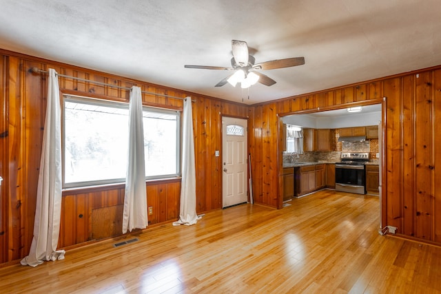 kitchen with tasteful backsplash, sink, stainless steel range with electric cooktop, ceiling fan, and light hardwood / wood-style flooring