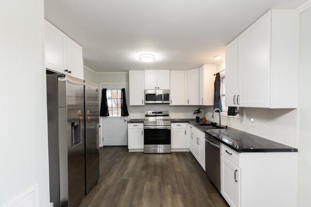 kitchen with stainless steel appliances, dark countertops, visible vents, a sink, and dark wood-style flooring