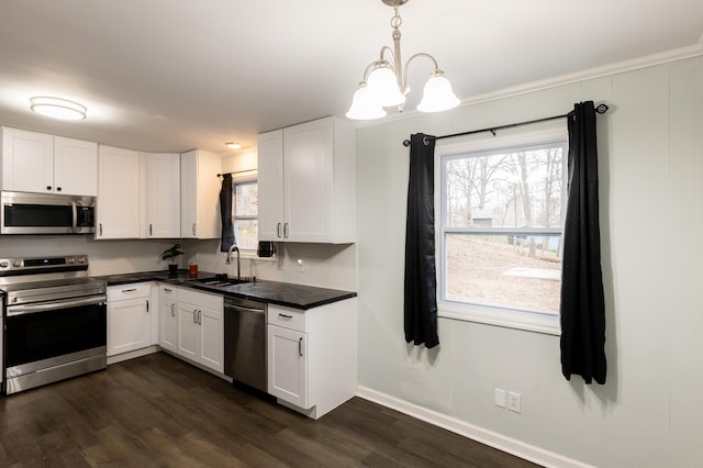 kitchen featuring stainless steel appliances, dark countertops, a sink, dark wood-type flooring, and white cabinetry