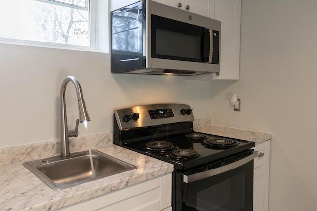 kitchen featuring sink, appliances with stainless steel finishes, light stone counters, and white cabinetry