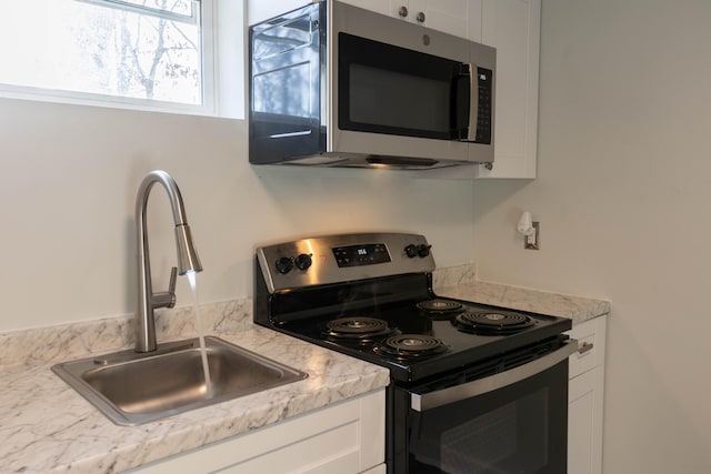 kitchen with a sink, stainless steel microwave, white cabinetry, light countertops, and electric stove