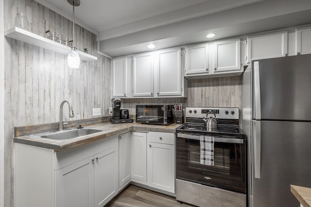 kitchen featuring light wood-type flooring, decorative light fixtures, sink, stainless steel appliances, and white cabinetry