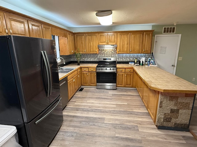 kitchen featuring kitchen peninsula, appliances with stainless steel finishes, light wood-type flooring, sink, and tile countertops