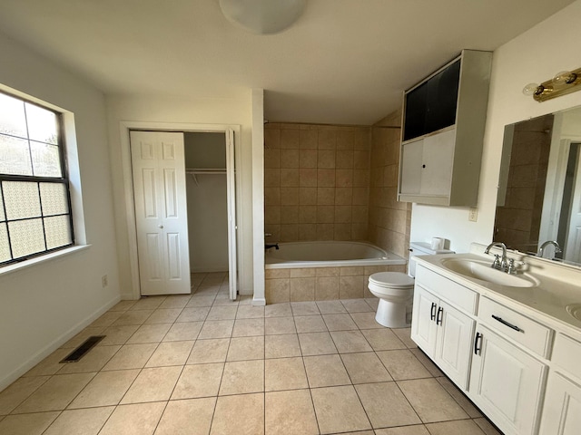 bathroom with tiled bath, tile patterned flooring, vanity, and toilet