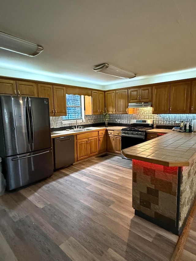 kitchen featuring backsplash, sink, hardwood / wood-style flooring, tile counters, and stainless steel appliances