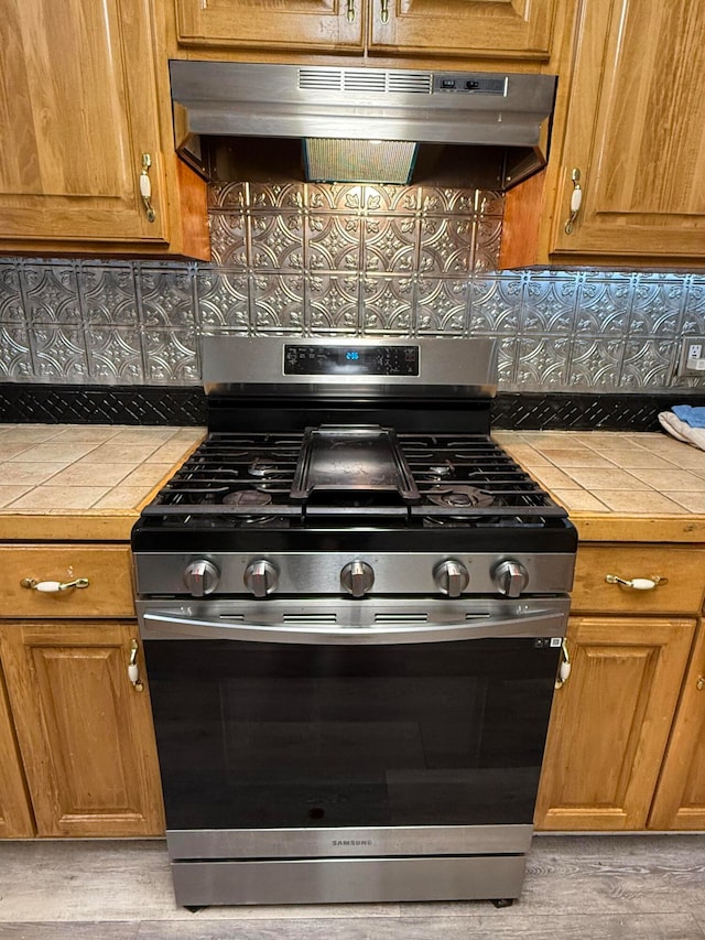 kitchen with tasteful backsplash, gas range, tile countertops, and ventilation hood