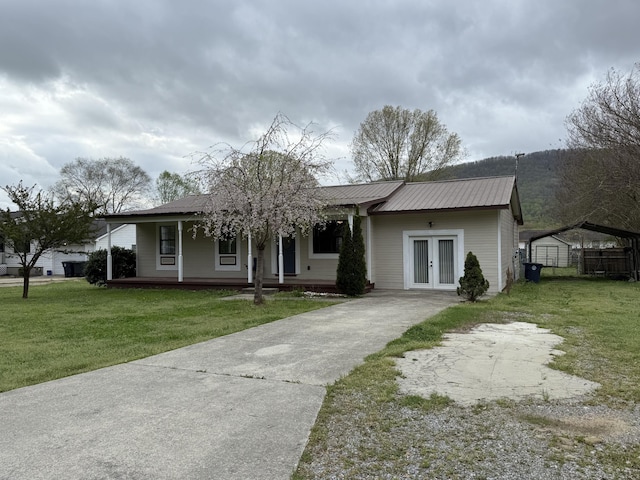 view of front of property with a front yard, covered porch, french doors, concrete driveway, and metal roof