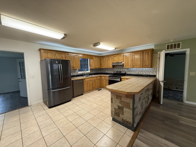 kitchen with visible vents, dishwasher, under cabinet range hood, stainless steel gas stove, and freestanding refrigerator