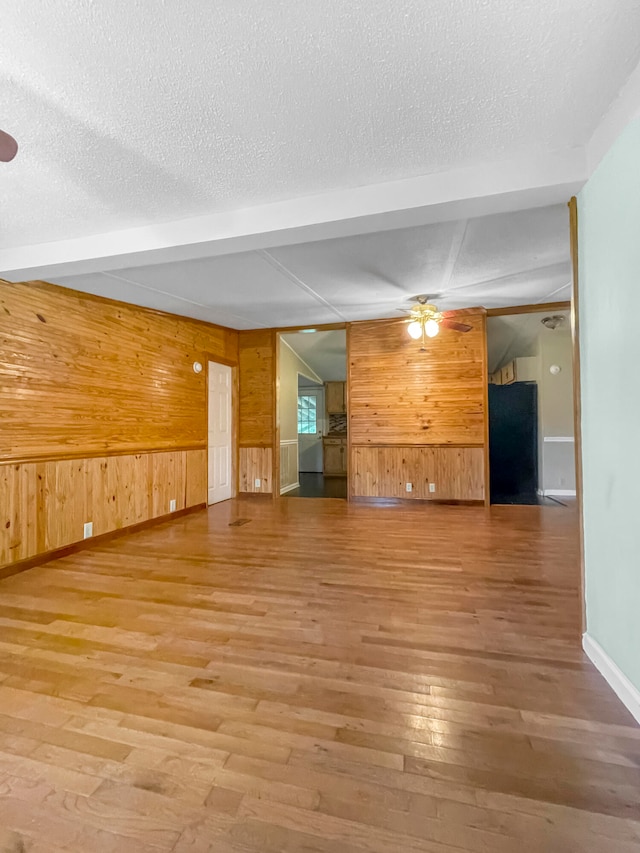 unfurnished living room featuring wood-type flooring, a textured ceiling, wood walls, and ceiling fan