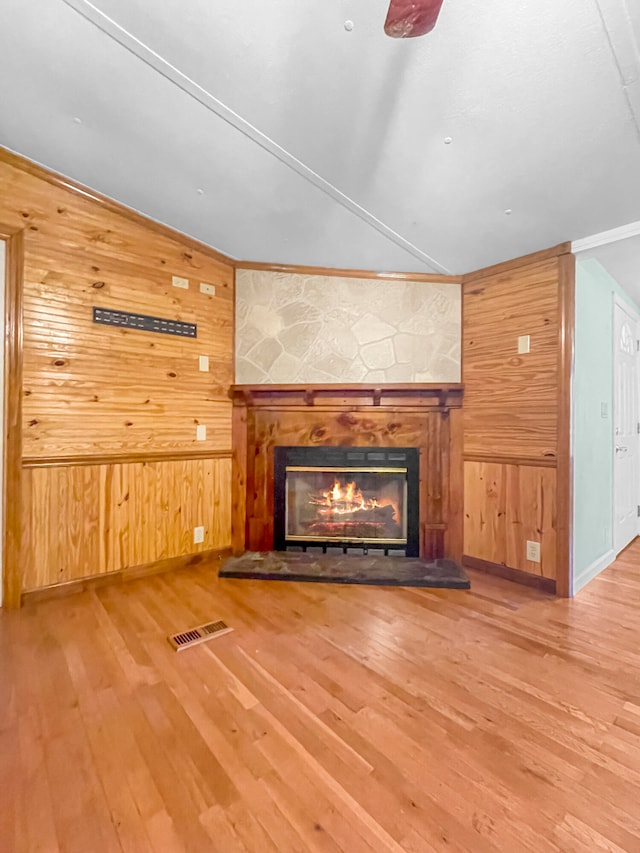 unfurnished living room with a stone fireplace, wooden walls, and hardwood / wood-style floors