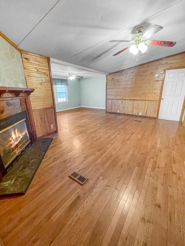 unfurnished living room featuring wood walls, ceiling fan, hardwood / wood-style floors, and a stone fireplace