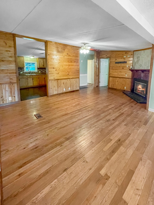 unfurnished living room with sink, wood walls, hardwood / wood-style floors, a stone fireplace, and ceiling fan