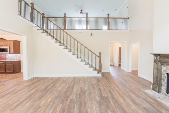 unfurnished living room with a high ceiling, a stone fireplace, light hardwood / wood-style floors, and ceiling fan