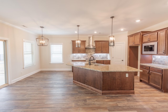 kitchen with wood-type flooring, wall chimney range hood, decorative light fixtures, light stone counters, and decorative backsplash