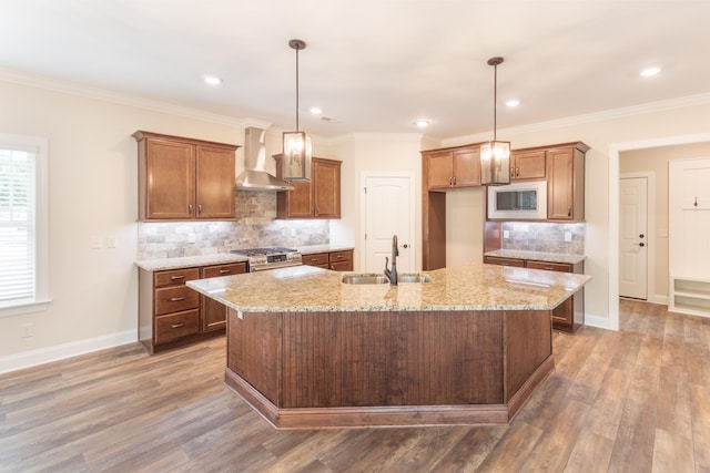 kitchen with light stone countertops, wall chimney range hood, sink, an island with sink, and hardwood / wood-style floors