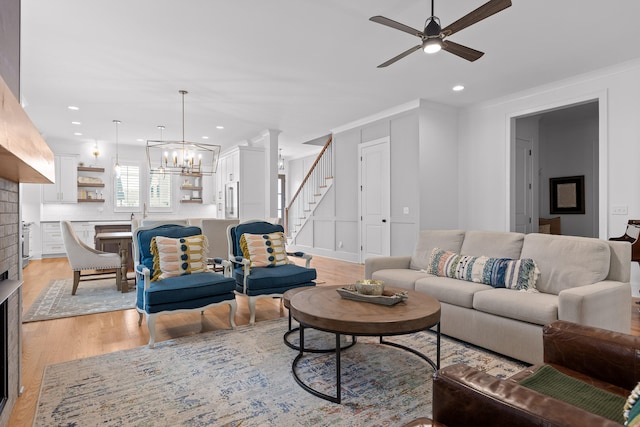 living room featuring ceiling fan with notable chandelier, light hardwood / wood-style floors, ornamental molding, and a brick fireplace