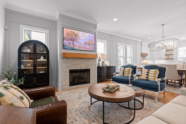 living room with crown molding, light hardwood / wood-style floors, an inviting chandelier, and a brick fireplace