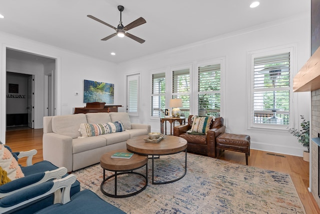 living room with light hardwood / wood-style flooring, ceiling fan, a fireplace, and ornamental molding