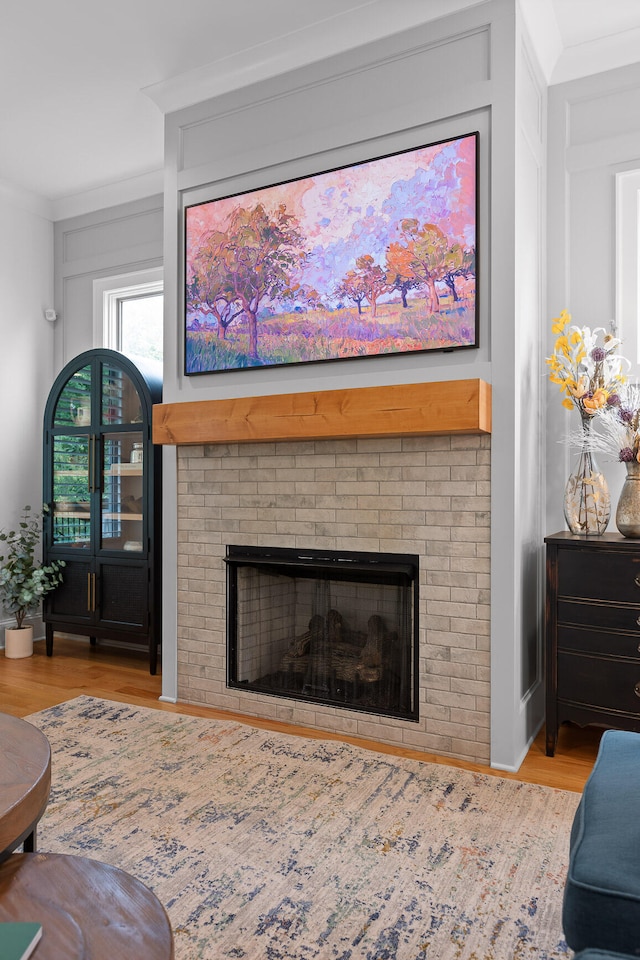 living room featuring ornamental molding, a brick fireplace, and light wood-type flooring