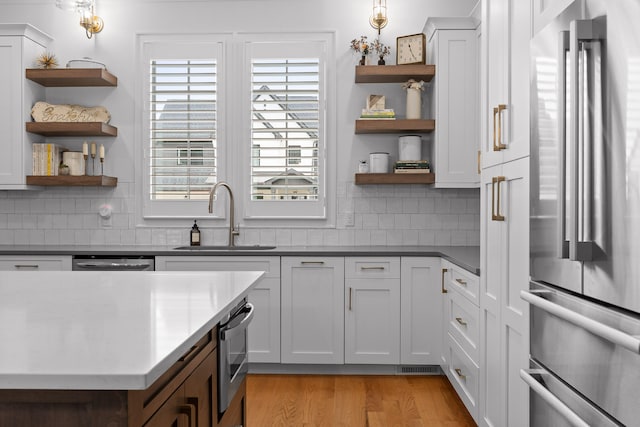 kitchen with light hardwood / wood-style floors, tasteful backsplash, sink, white cabinets, and stainless steel fridge