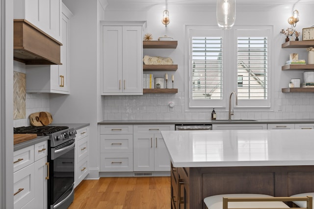 kitchen with white cabinetry, a breakfast bar, stainless steel gas range oven, pendant lighting, and sink