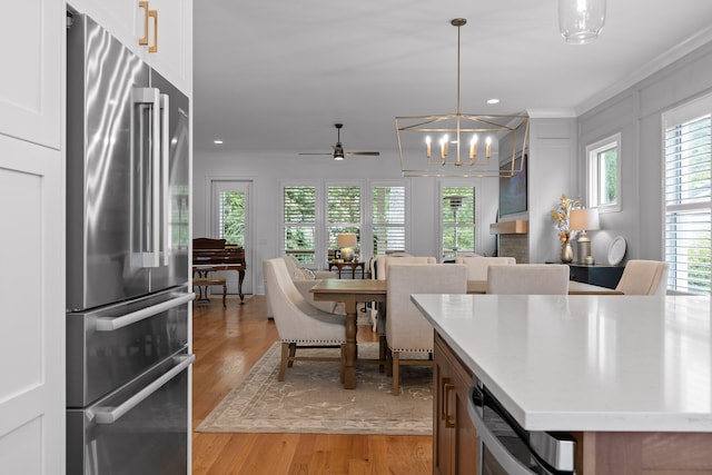 kitchen with light hardwood / wood-style floors, ceiling fan with notable chandelier, hanging light fixtures, a kitchen island, and high end fridge