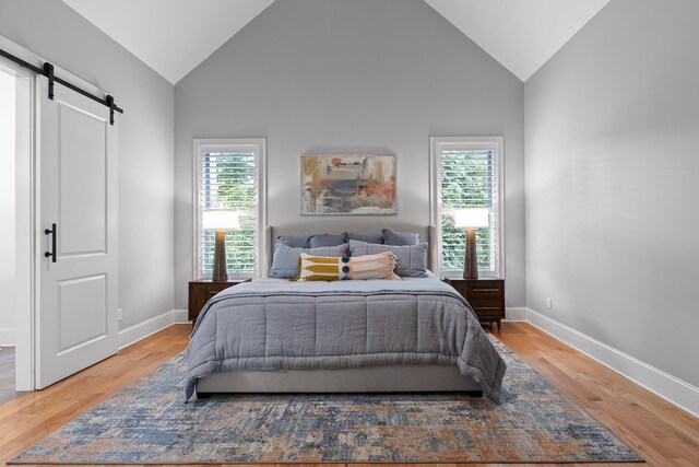 bedroom with hardwood / wood-style floors, high vaulted ceiling, and a barn door