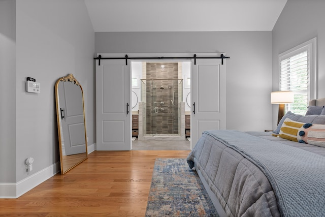 bedroom with vaulted ceiling, light hardwood / wood-style floors, ensuite bath, and a barn door