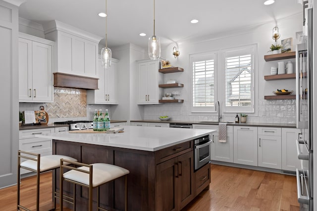 kitchen with white cabinetry, a breakfast bar area, hanging light fixtures, a center island, and light wood-type flooring