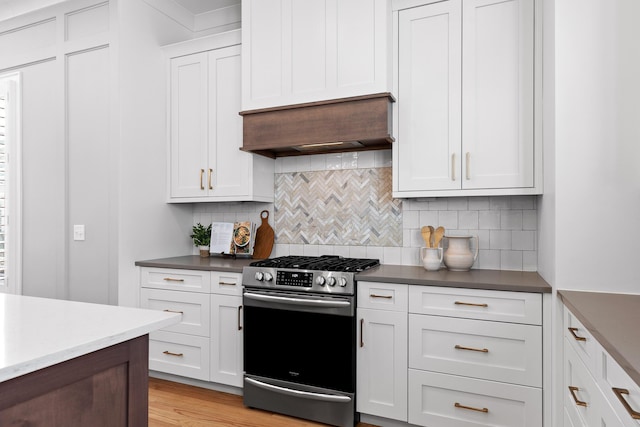 kitchen featuring custom exhaust hood, gas stove, white cabinets, and backsplash