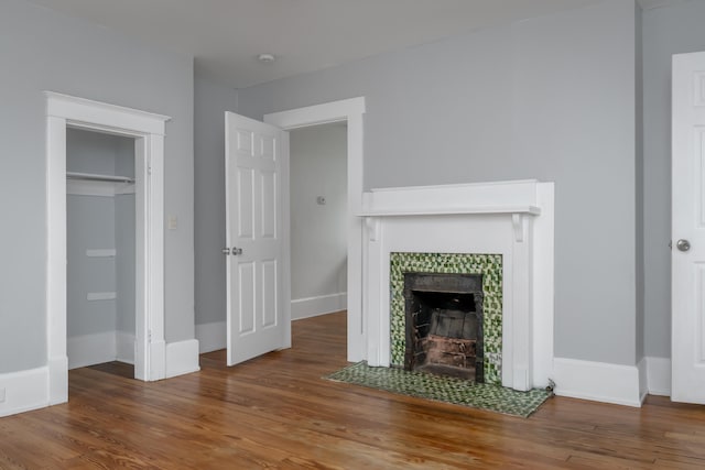 unfurnished living room with wood-type flooring and a tiled fireplace