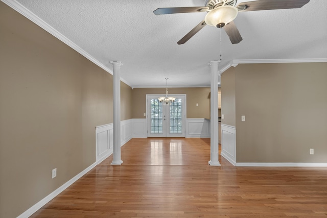 spare room featuring ceiling fan with notable chandelier, ornate columns, crown molding, light hardwood / wood-style flooring, and french doors