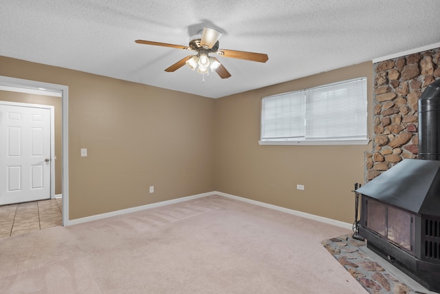 unfurnished living room featuring light carpet, a wood stove, ceiling fan, and a textured ceiling