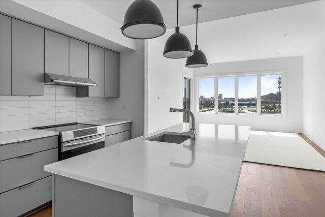 kitchen featuring electric stove, pendant lighting, a kitchen island with sink, and sink