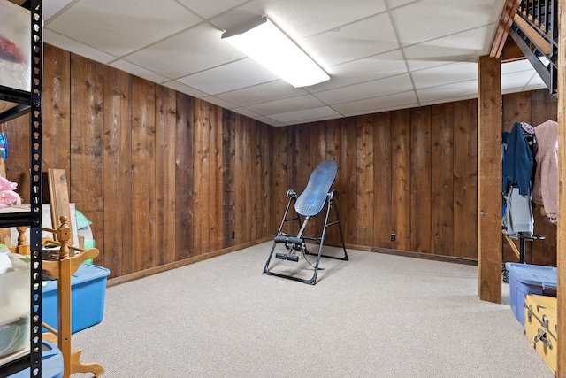 workout room with light colored carpet, a drop ceiling, and wood walls