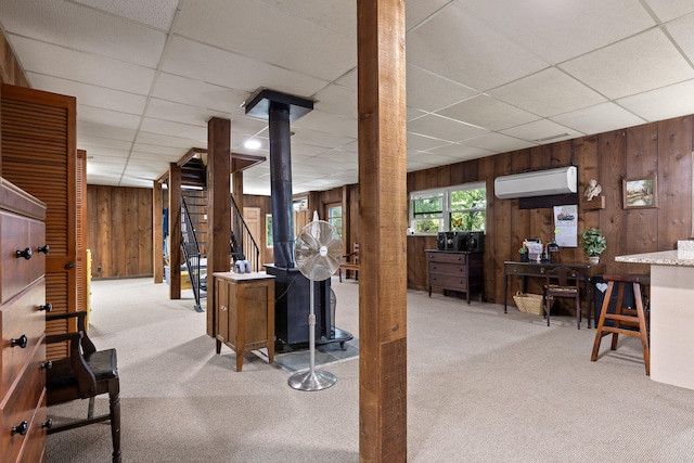 interior space with a paneled ceiling, wood walls, light carpet, and a wall mounted air conditioner