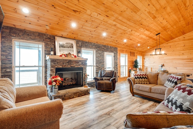 living room featuring light wood-type flooring, vaulted ceiling, wood walls, a stone fireplace, and wooden ceiling