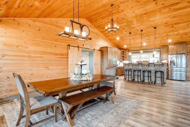 dining area featuring a barn door, light hardwood / wood-style floors, wood walls, and high vaulted ceiling