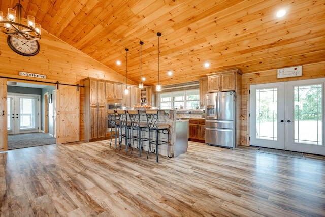 kitchen featuring hanging light fixtures, high vaulted ceiling, appliances with stainless steel finishes, a barn door, and a wealth of natural light