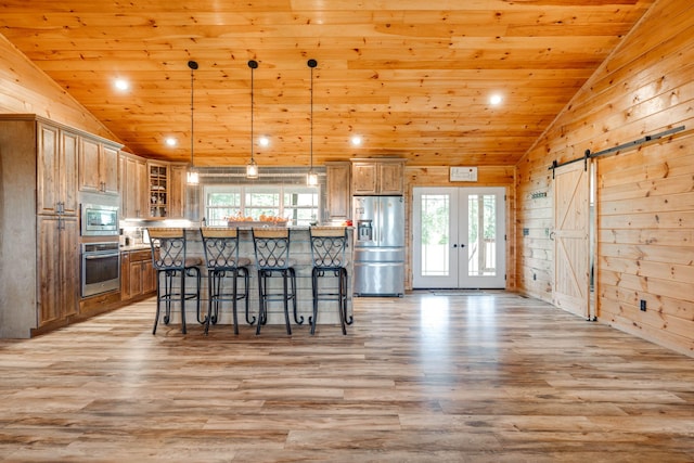 kitchen featuring pendant lighting, light hardwood / wood-style floors, wood walls, a barn door, and stainless steel appliances