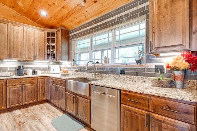 kitchen with vaulted ceiling, backsplash, light stone countertops, stainless steel dishwasher, and sink