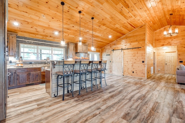 kitchen featuring light hardwood / wood-style flooring, wood walls, decorative light fixtures, and a barn door