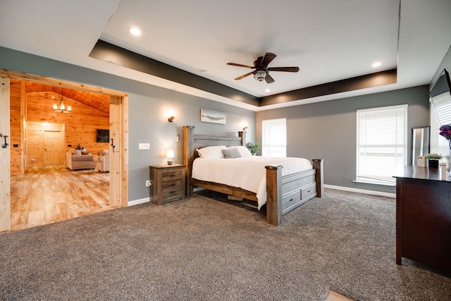 bedroom with ceiling fan, wood walls, dark colored carpet, and multiple windows