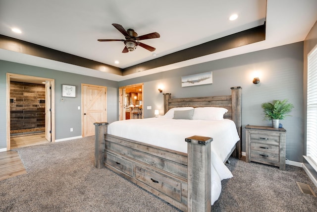 bedroom with dark colored carpet, ceiling fan, a tray ceiling, and ensuite bathroom