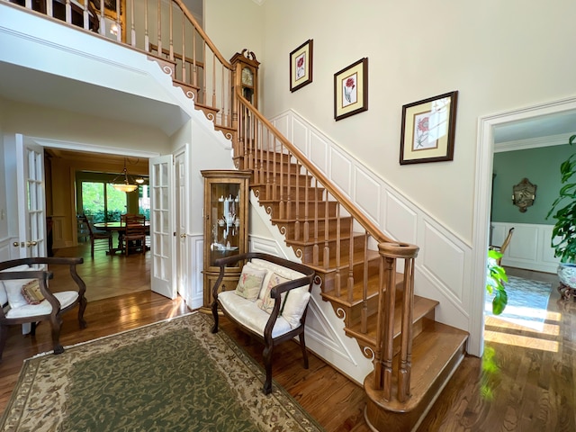 stairway with hardwood / wood-style flooring, crown molding, a high ceiling, and french doors