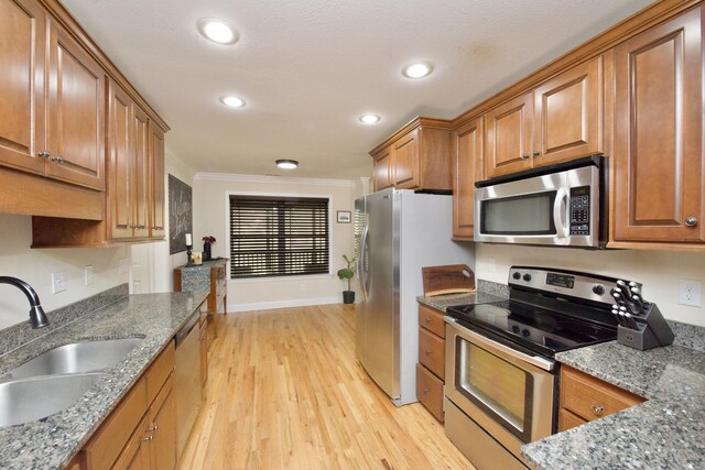 kitchen with stainless steel appliances, light wood-type flooring, dark stone counters, ornamental molding, and sink